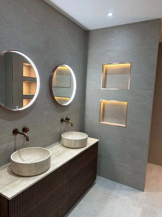 Moderne badkamer met dubbele wastafel, ronde spiegels en grijze tegels.