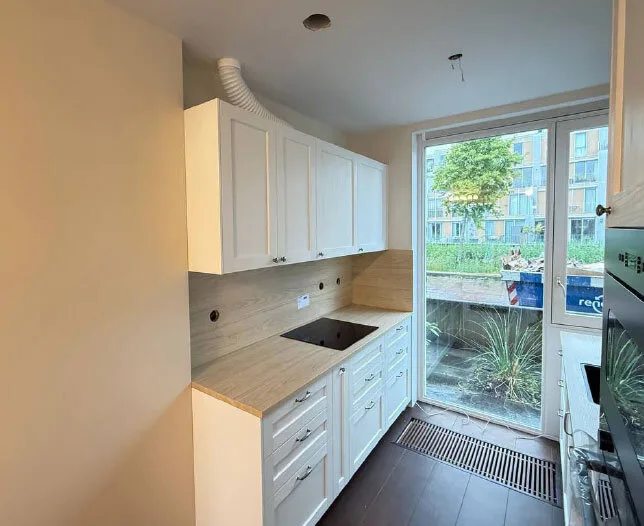 Moderne keukenrenovatie met witte kasten, houten blad en grote raampartij.