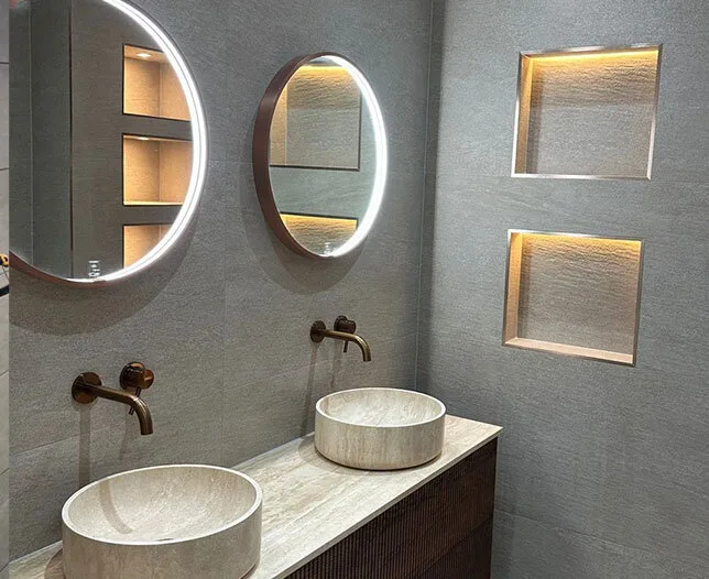 Moderne badkamer met dubbele wastafel, ronde spiegels en inbouw nissen met verlichting.